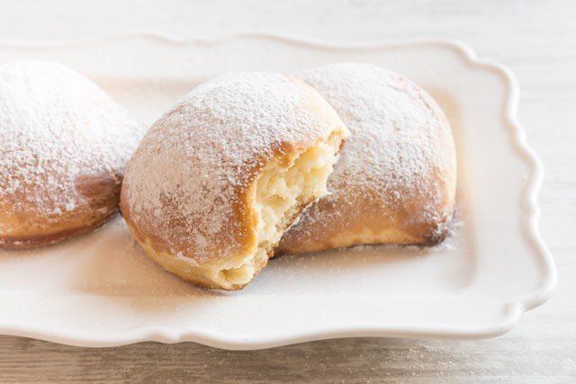 Due ciambelle con zucchero a velo su un piatto bianco e un morso da una di esse.