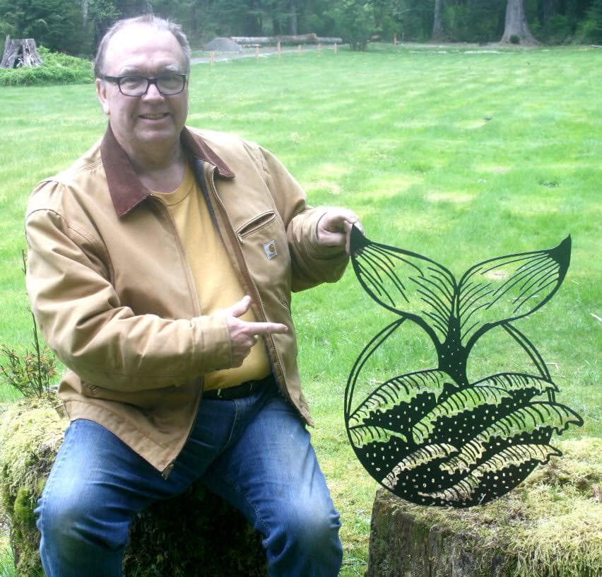 Man in tan jacket holding a large black wire sculpture of a plant in a grassy park