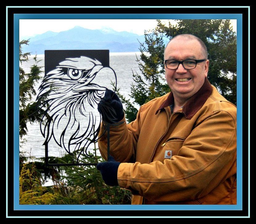 Man smiling while holding a black-and-white eagle drawing outdoors by a lake