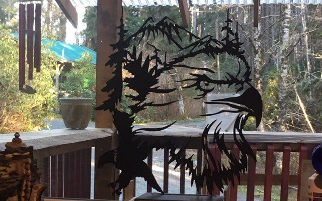 Black metal bird-and-tree sculpture on a porch, silhouetted against a wooded yard with red railing.