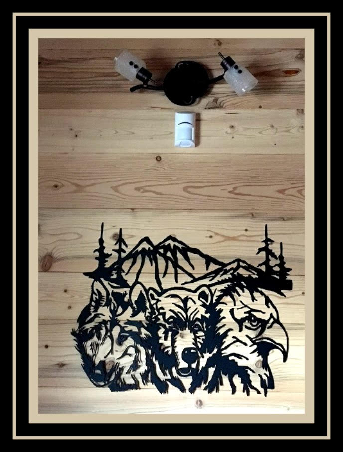 Wooden wall art with black mountain and wolf silhouette on light wood, under a small light fixture.