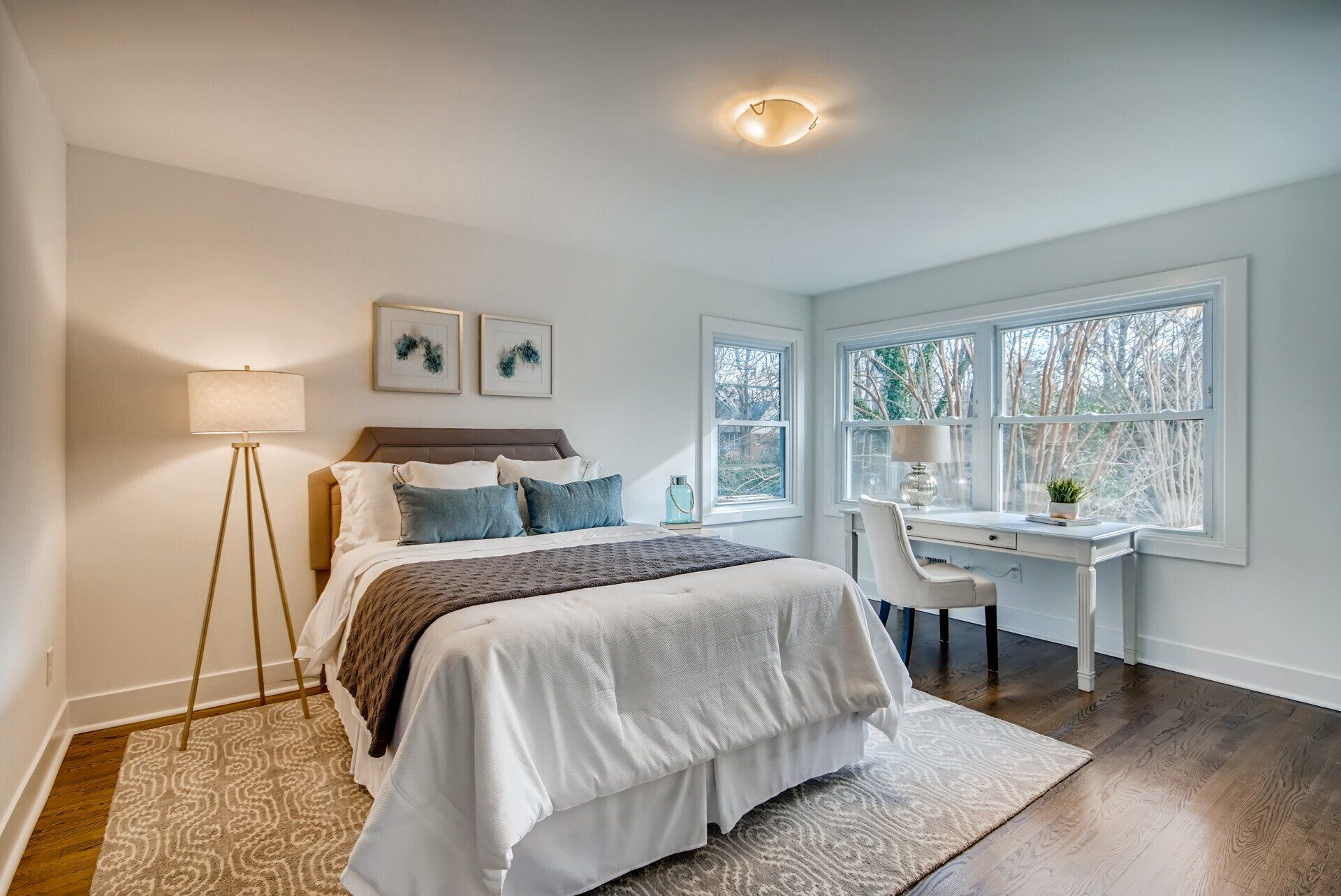 A bedroom with a bed , desk , lamp and windows.