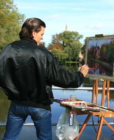 A man in a black jacket is painting a picture on an easel
