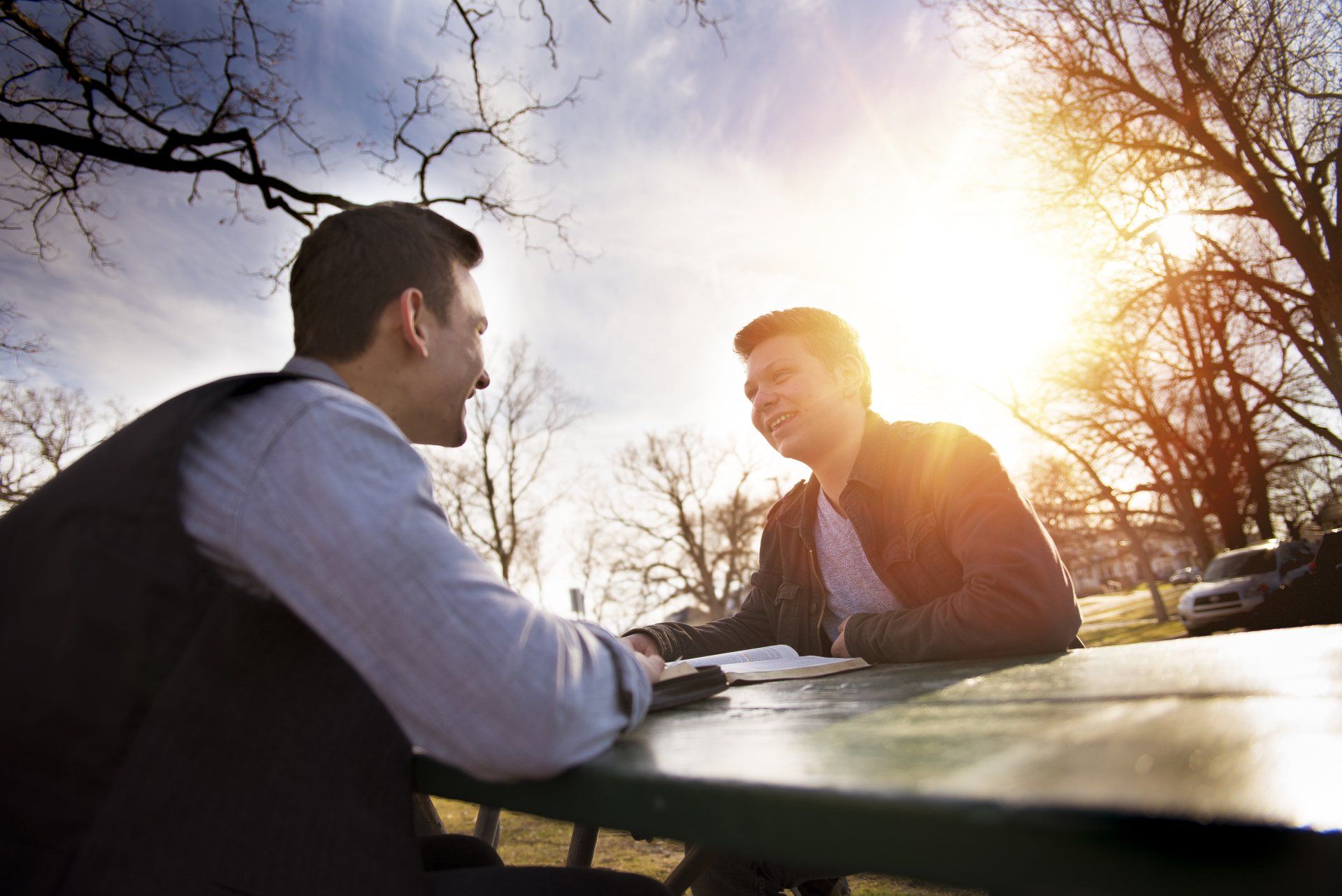 Two gentlemen on a park bench near sunset, discussing the Bible, with their Bibles opened.