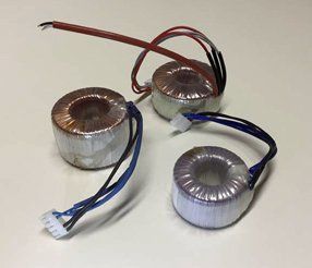 Tre trasformatori toroidali con fili e connettori colorati.
