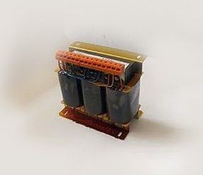 Un trasformatore trifase con bobine nere, morsettiera rossa e componenti metallici dorati.