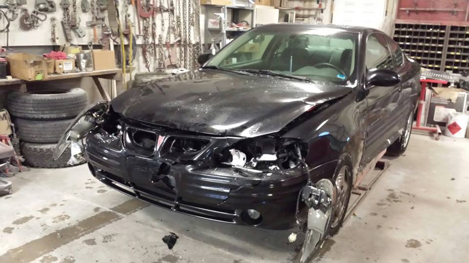 a black car with a damaged front end sits in a garage