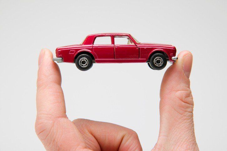 A person is holding a red toy car between their fingers.
