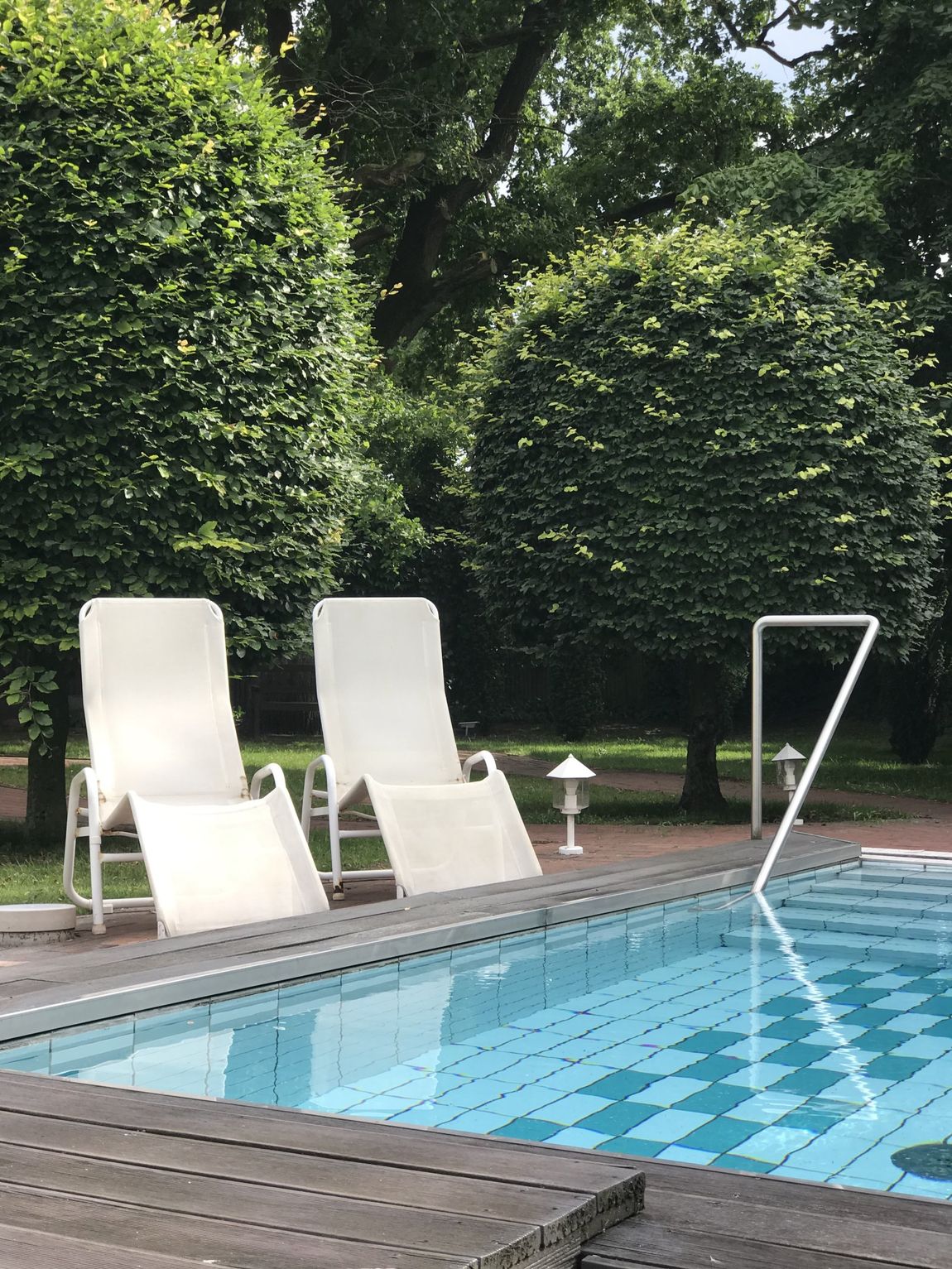Zwei weiße Liegestühle stehen neben einem Swimmingpool.