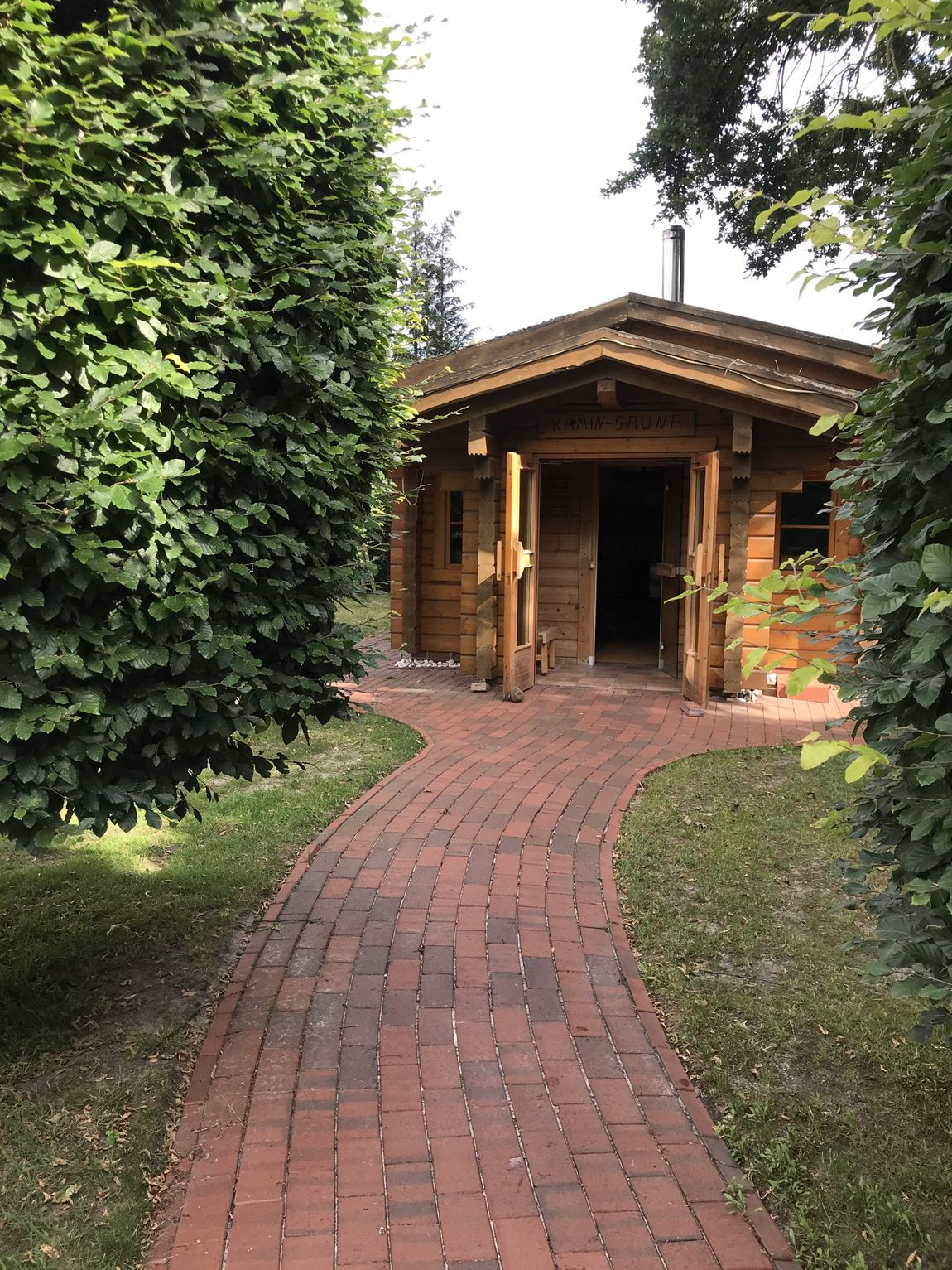 Ein Ziegelweg führt zu einem von Bäumen umgebenen Holzhaus