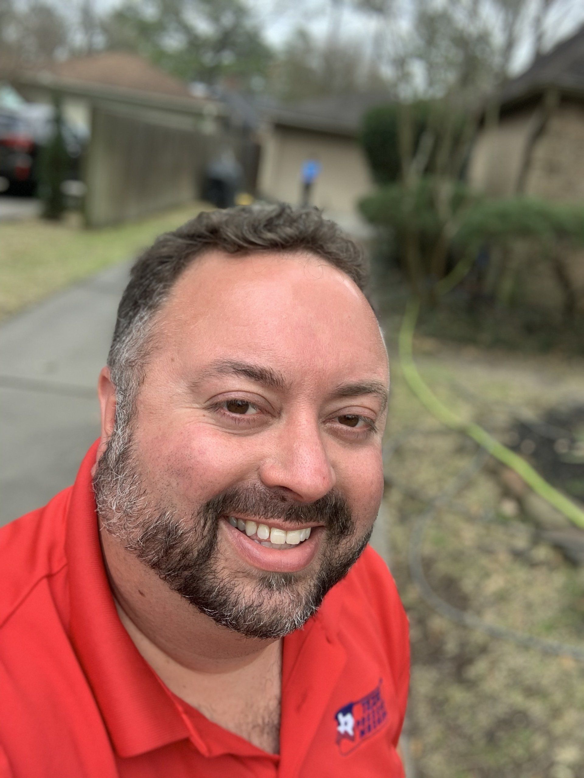A man with a beard is wearing a red shirt and smiling.