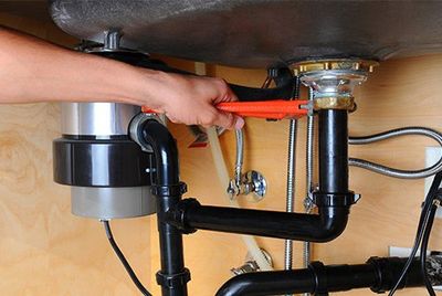 Tankless Water Heater — Plumber Using Wrench Under Kitchen Sink in Goldsboro, NC Tankless Water Heater — Plumber Using Wrench Under Kitchen Sink in Goldsboro, NC
