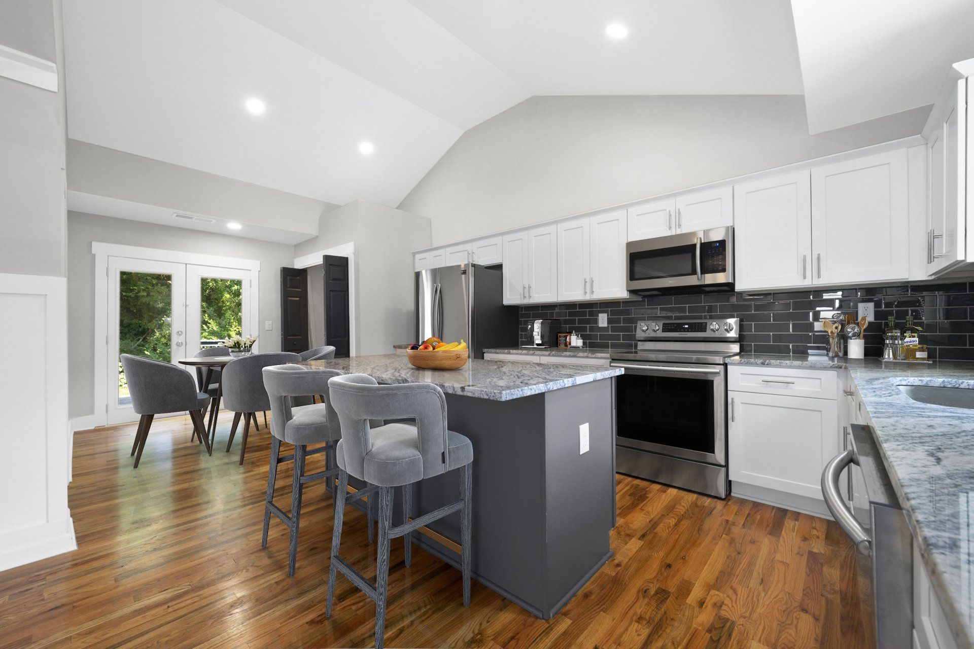 A kitchen with white cabinets , stainless steel appliances , granite counter tops and hardwood floors.