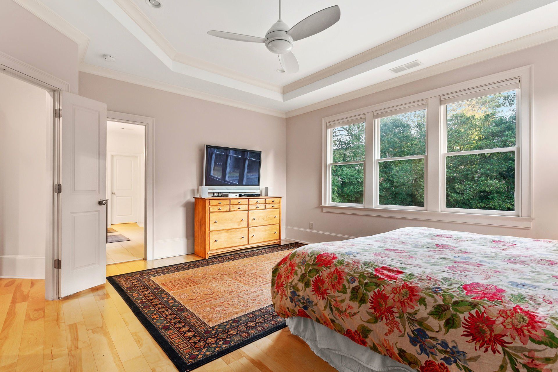 A bedroom with a bed , dresser , television and ceiling fan.