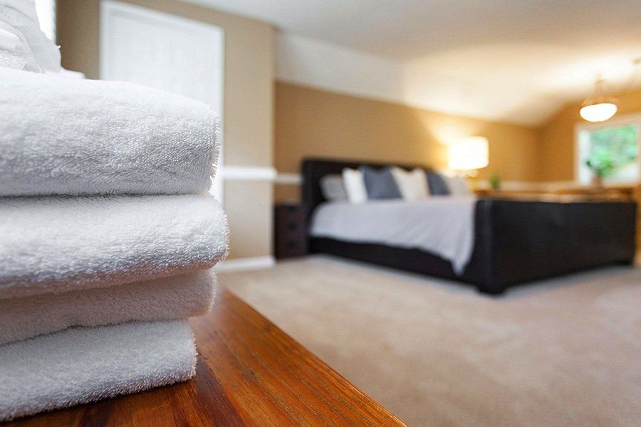 A stack of towels is sitting on a wooden table in front of a bed in a hotel room.