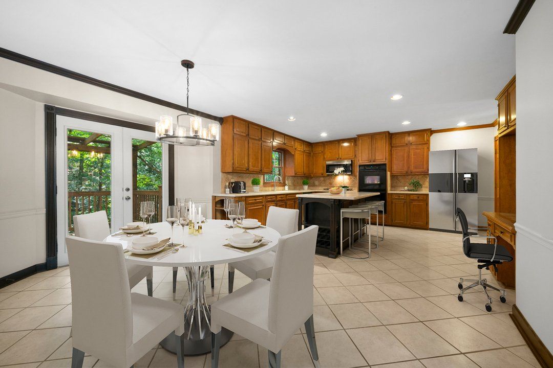 A dining room with a table and chairs and a kitchen in the background.