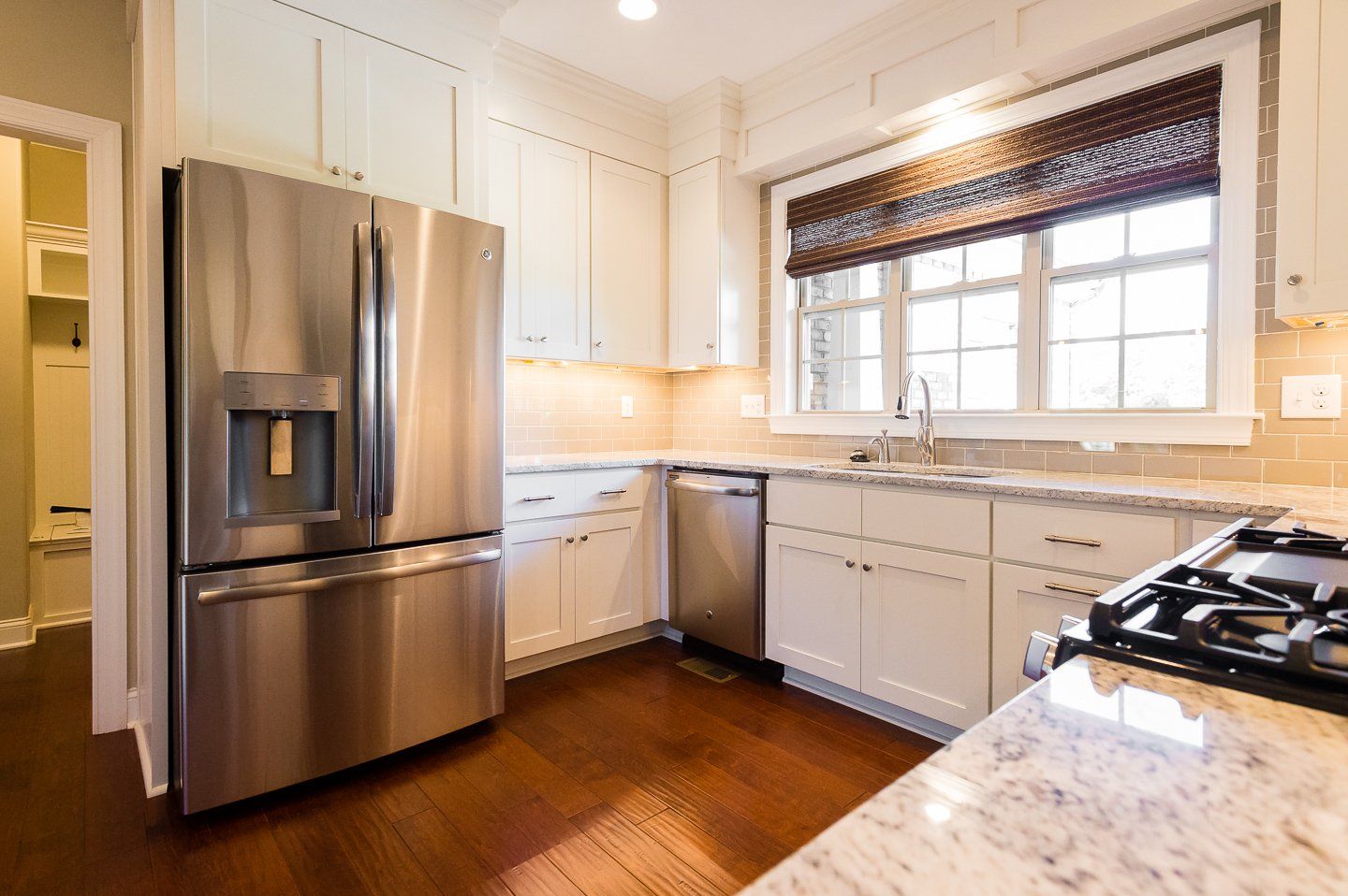 Bright modern kitchen with stainless steel fridge, white cabinets, granite counters, and window over sink