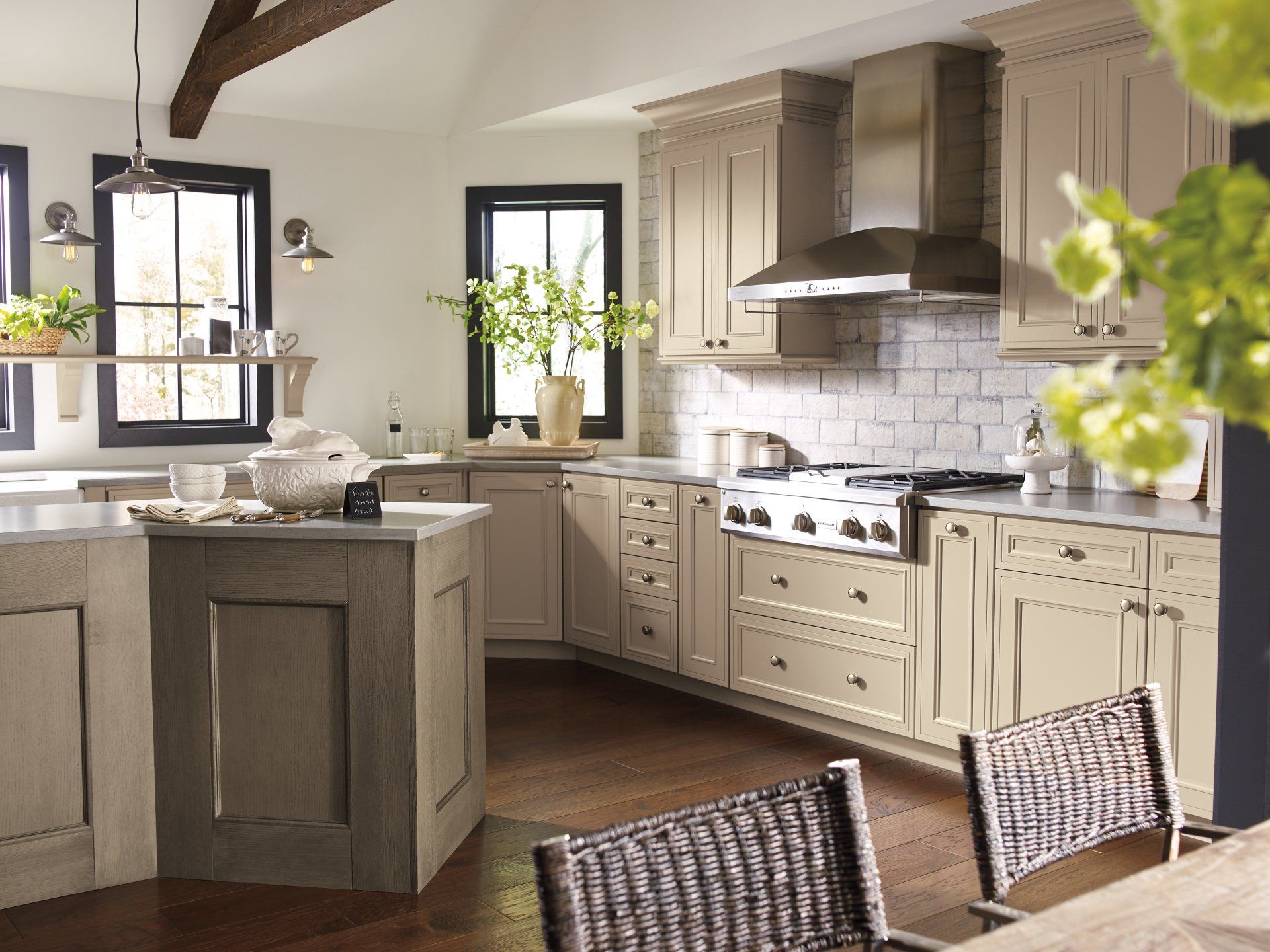 Bright, modern kitchen with island, cream cabinets, stainless range hood, and wicker chairs in the foreground