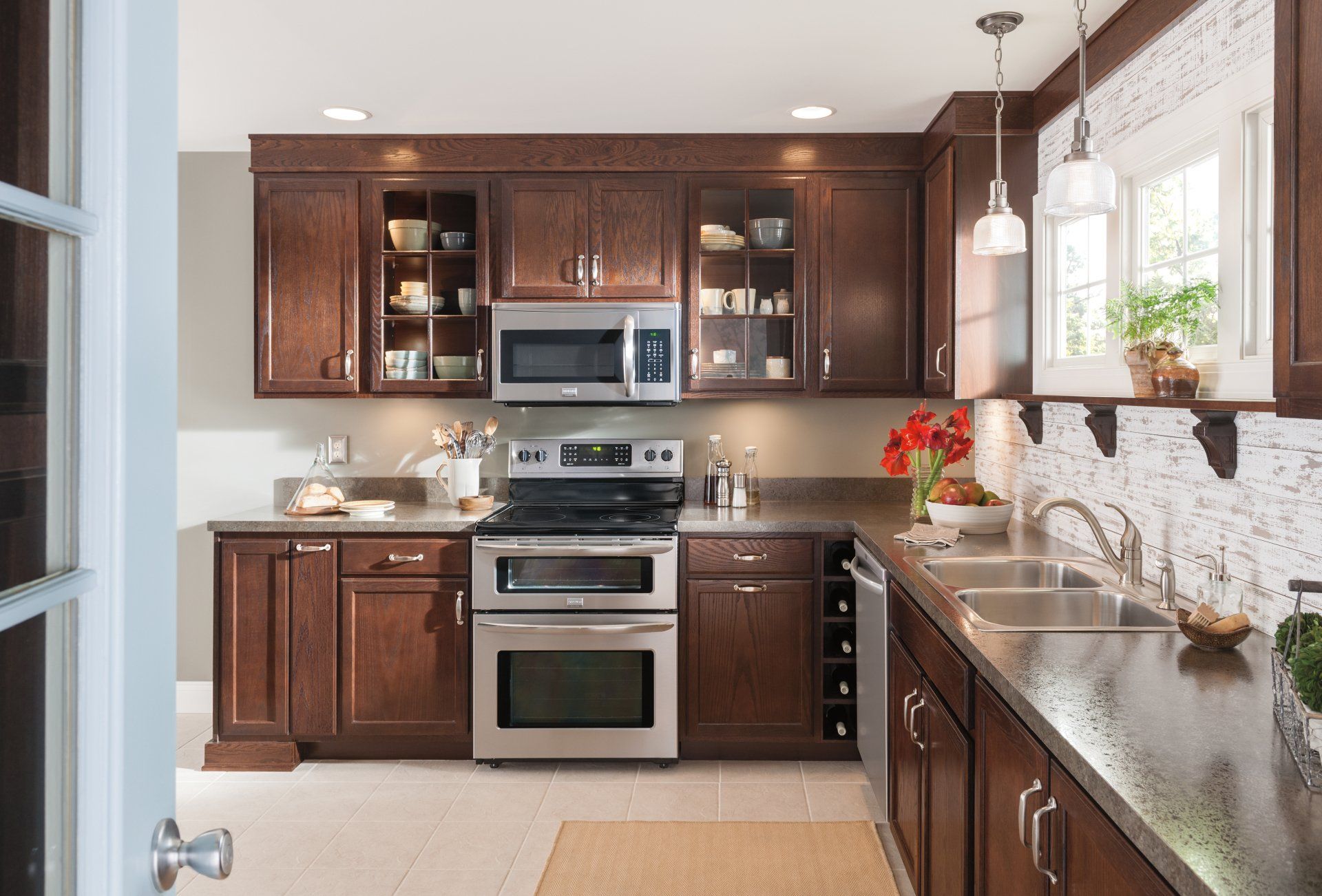 Modern kitchen with dark wood cabinets, stainless steel appliances, and a long countertop by a bright window.
