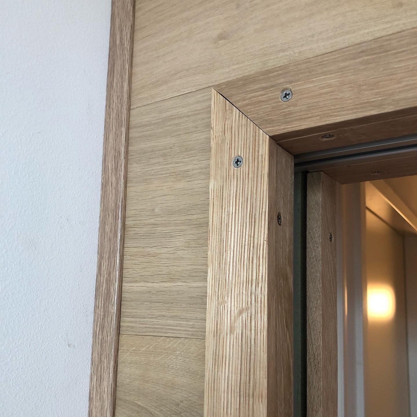 Houten deurkozijn met zichtbare schroefkoppen, grenzend aan een witte muur.