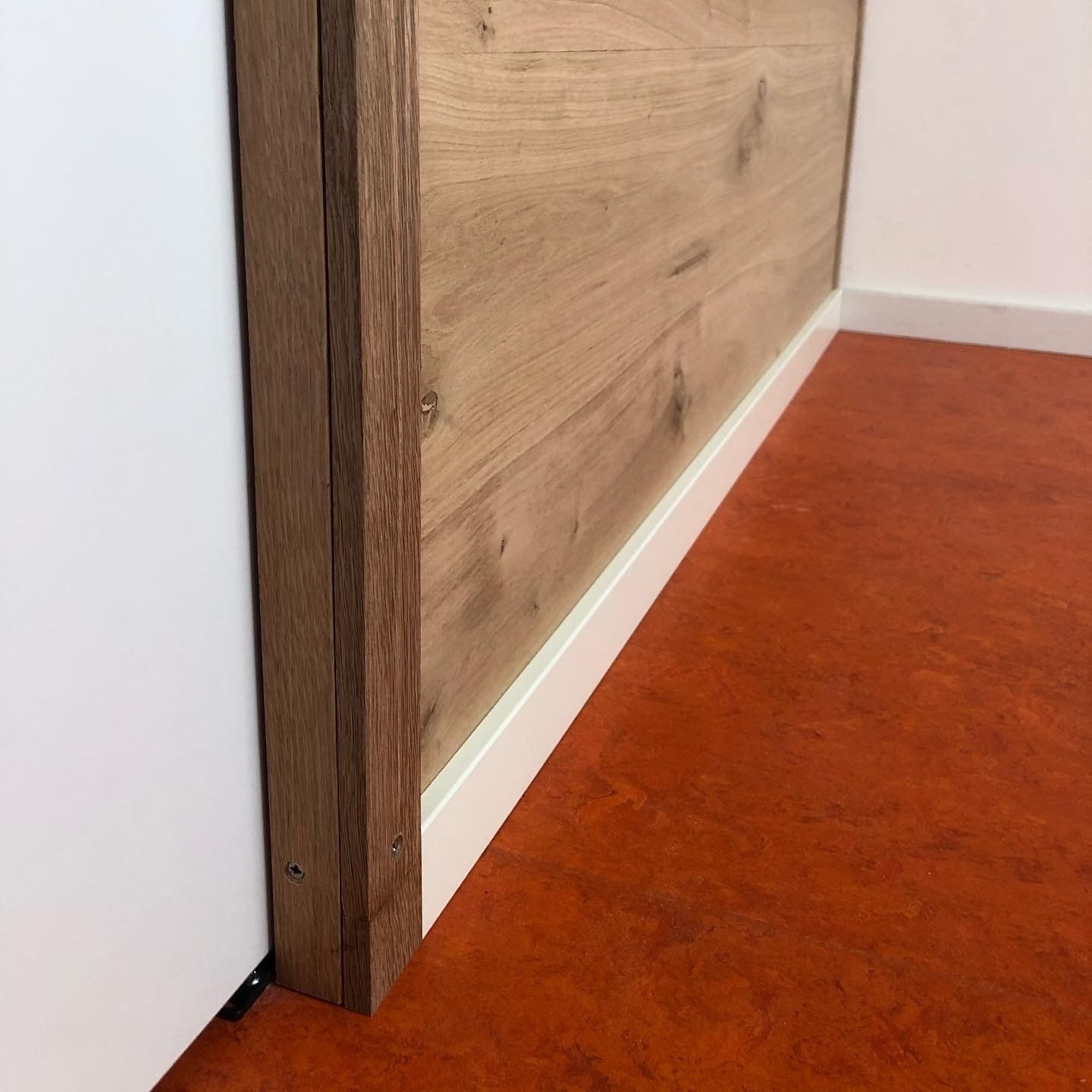 Houten lambrisering tegen een witte muur met witte plinten op een oranje vloer.