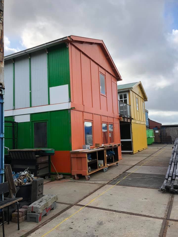 Kleurrijke, gestapelde containers. Oranje, groene en gele buitenkanten staan op een geplaveid terrein.