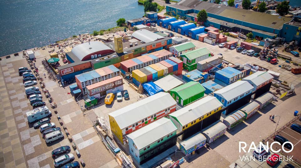 Luchtfoto van kleurrijke zeecontainers en gebouwen op een kade en een wateroppervlak op de achtergrond.