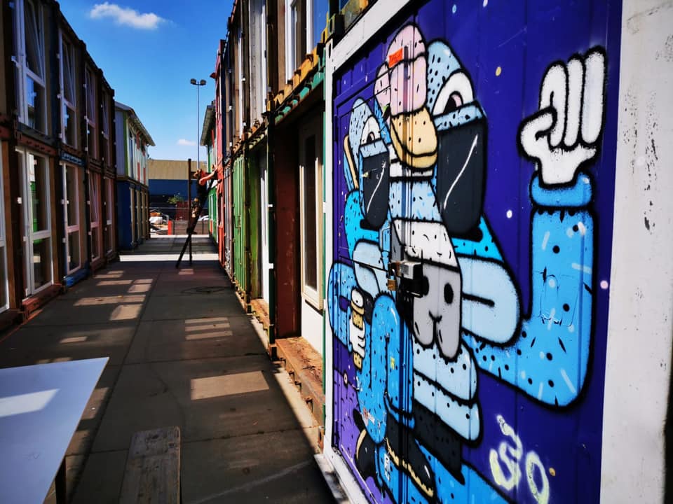 Een kleurrijk steegje met graffiti op een blauwe muur. Een helderblauwe lucht erboven.