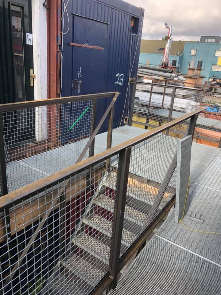 Metalen trap die leidt naar een blauwe containerdeur met een metalen platform en leuning.