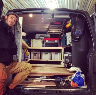 Martes zit in een busje vol gereedschap en opbergruimte; hij draagt ​​een bruine broek en het gereedschap is zichtbaar.