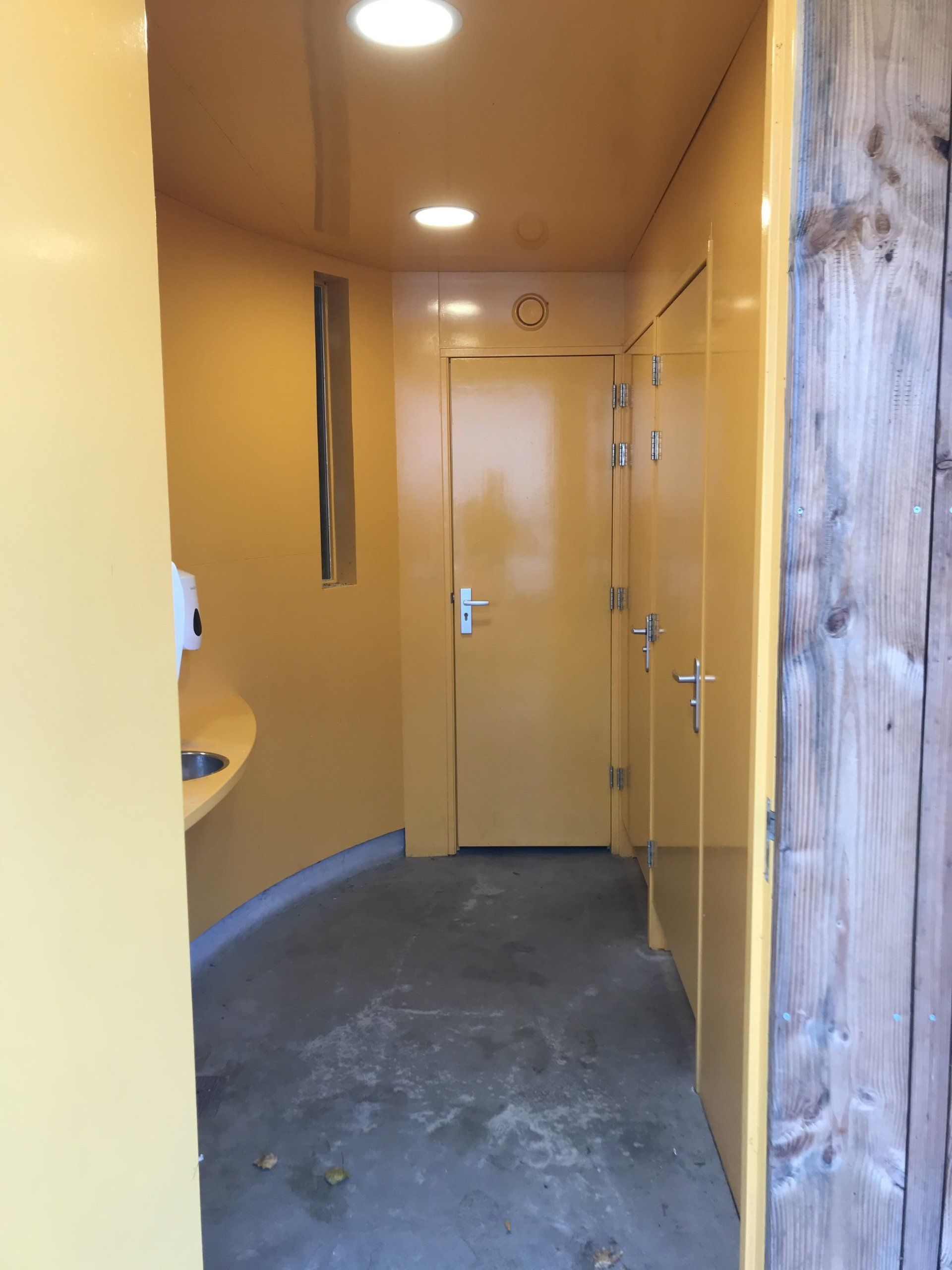 Geel openbaar toilet met deuren en een wastafel.