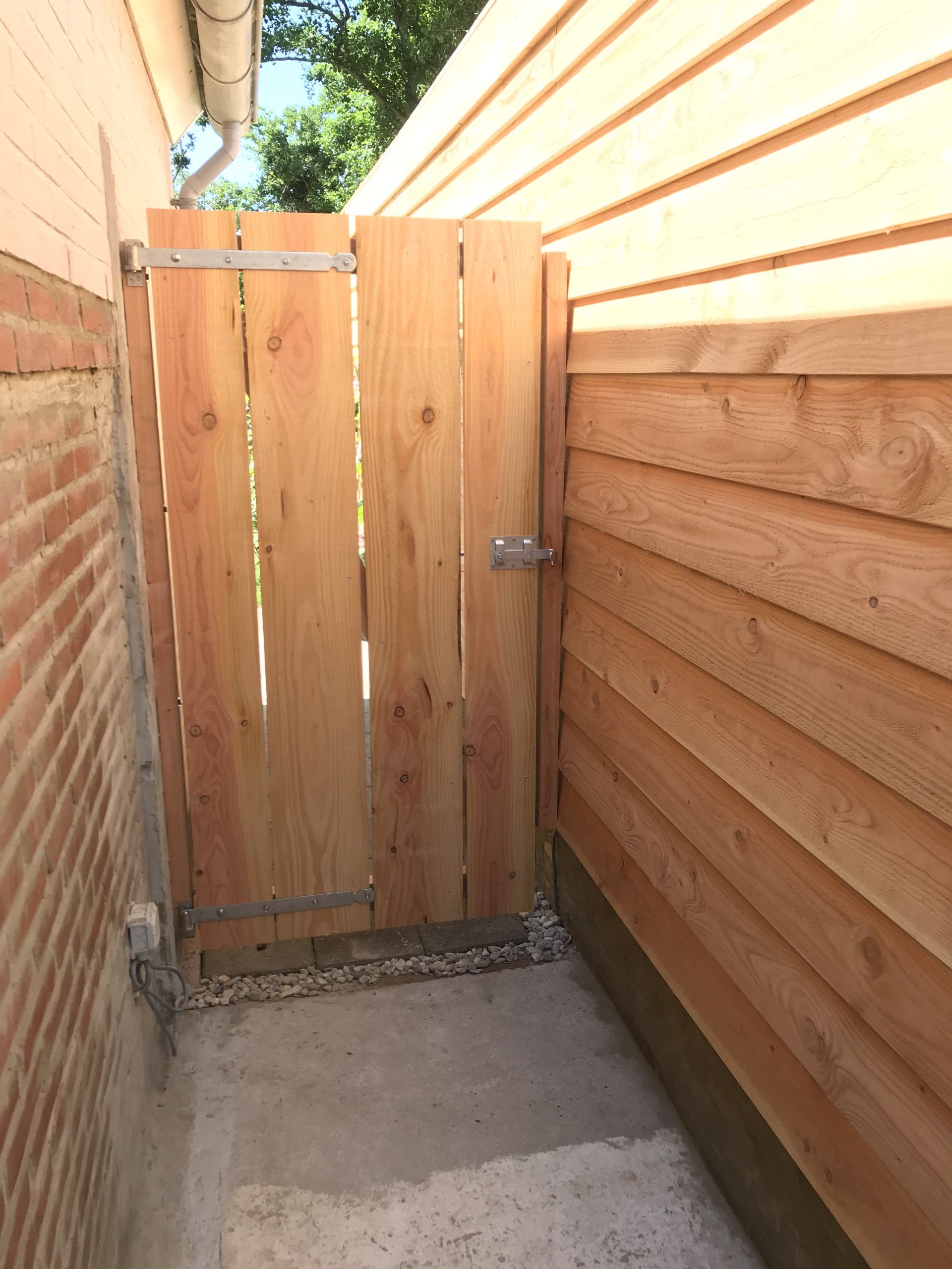 Houten poort in een steegje, tussen een bakstenen muur en houten gevelbekleding.
