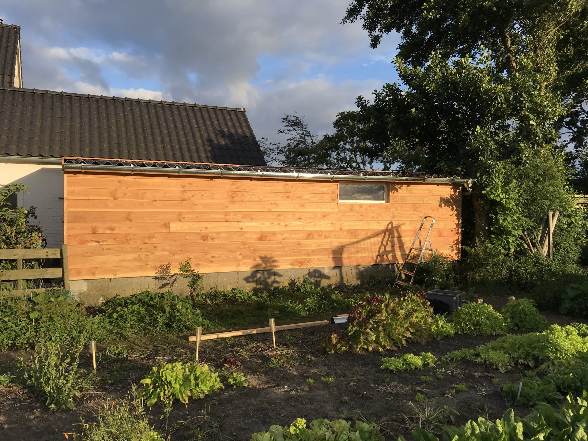 Houten schuur met tuin ervoor, onder een bewolkte hemel.