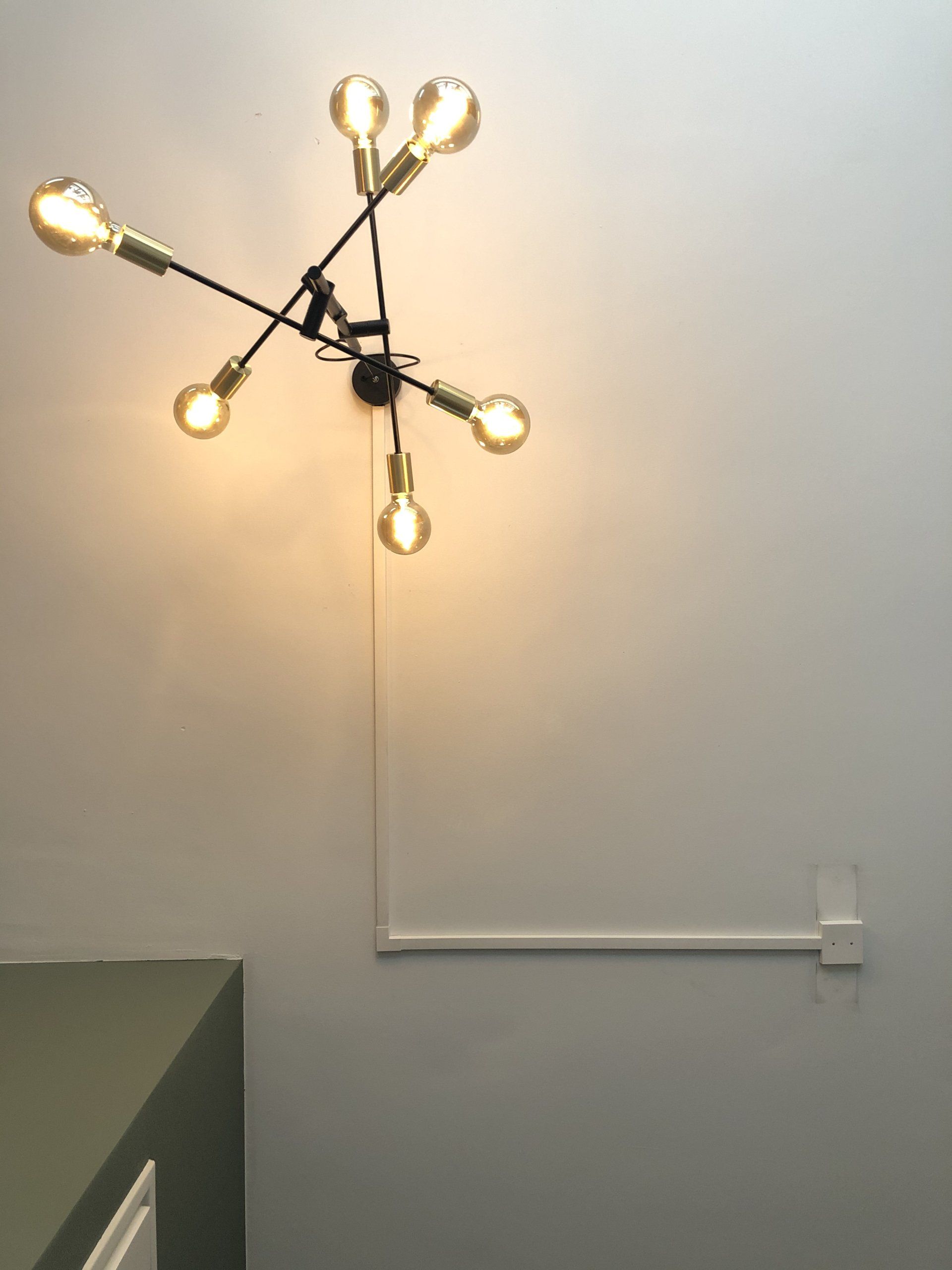 Moderne zwarte lamp met Edison-lampen op een witte muur, inclusief snoer en kabelgoot naar het stopcontact.