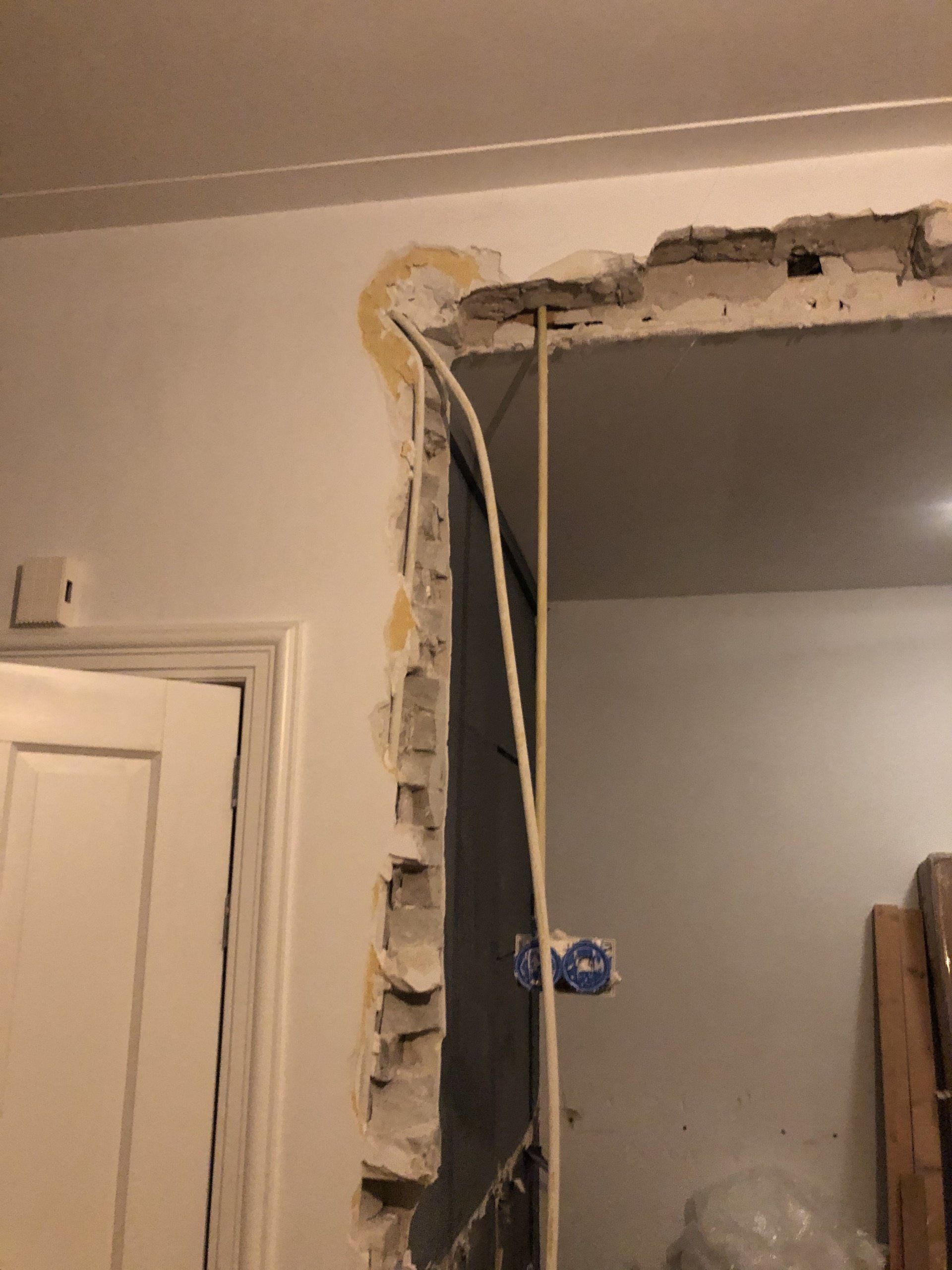 Muuropening met zichtbare bedrading en stucwerk, naast een deuropening.
