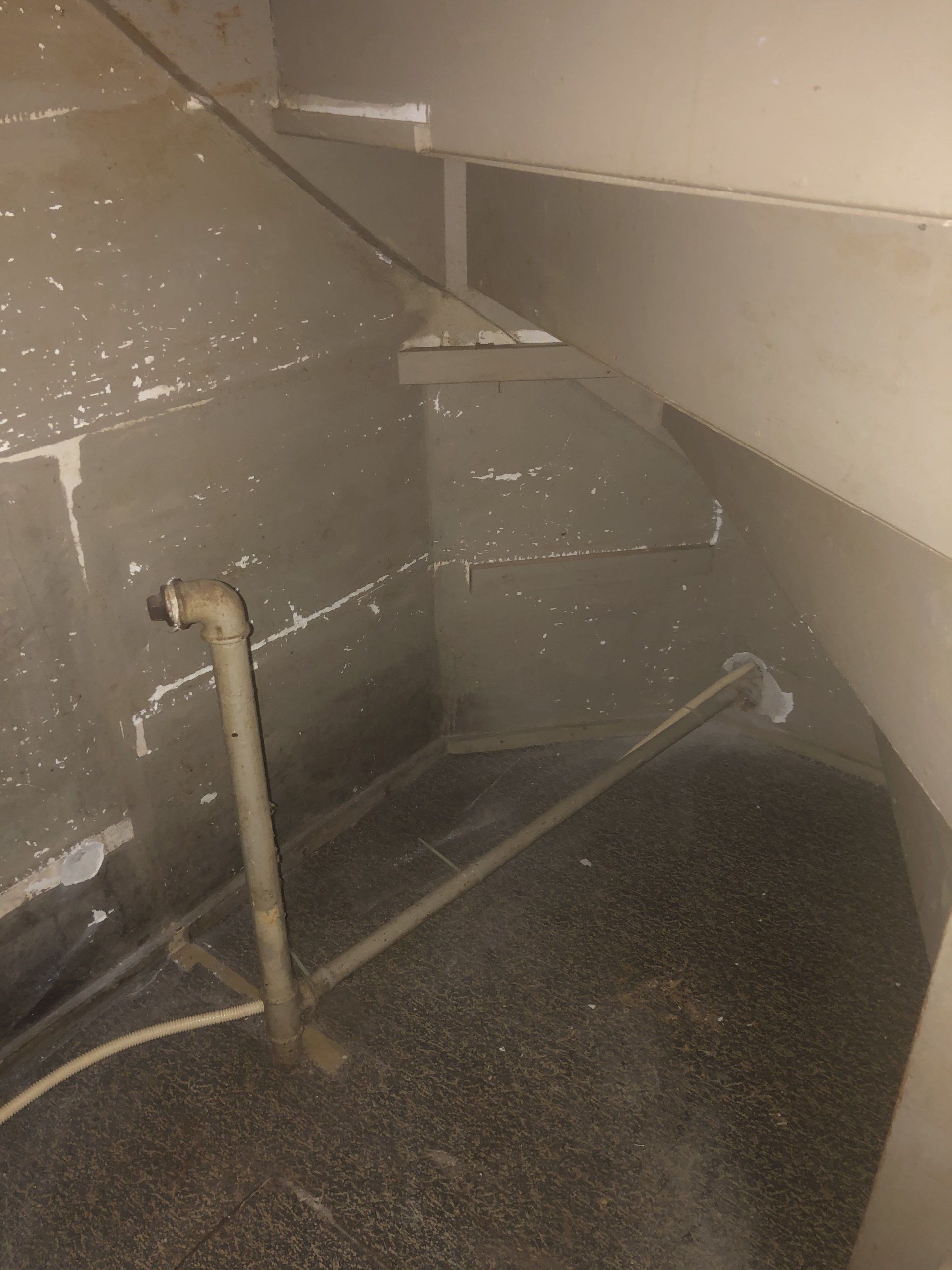 Interieurfoto van een donkere kamer met zichtbare waterleidingen en metalen balken.