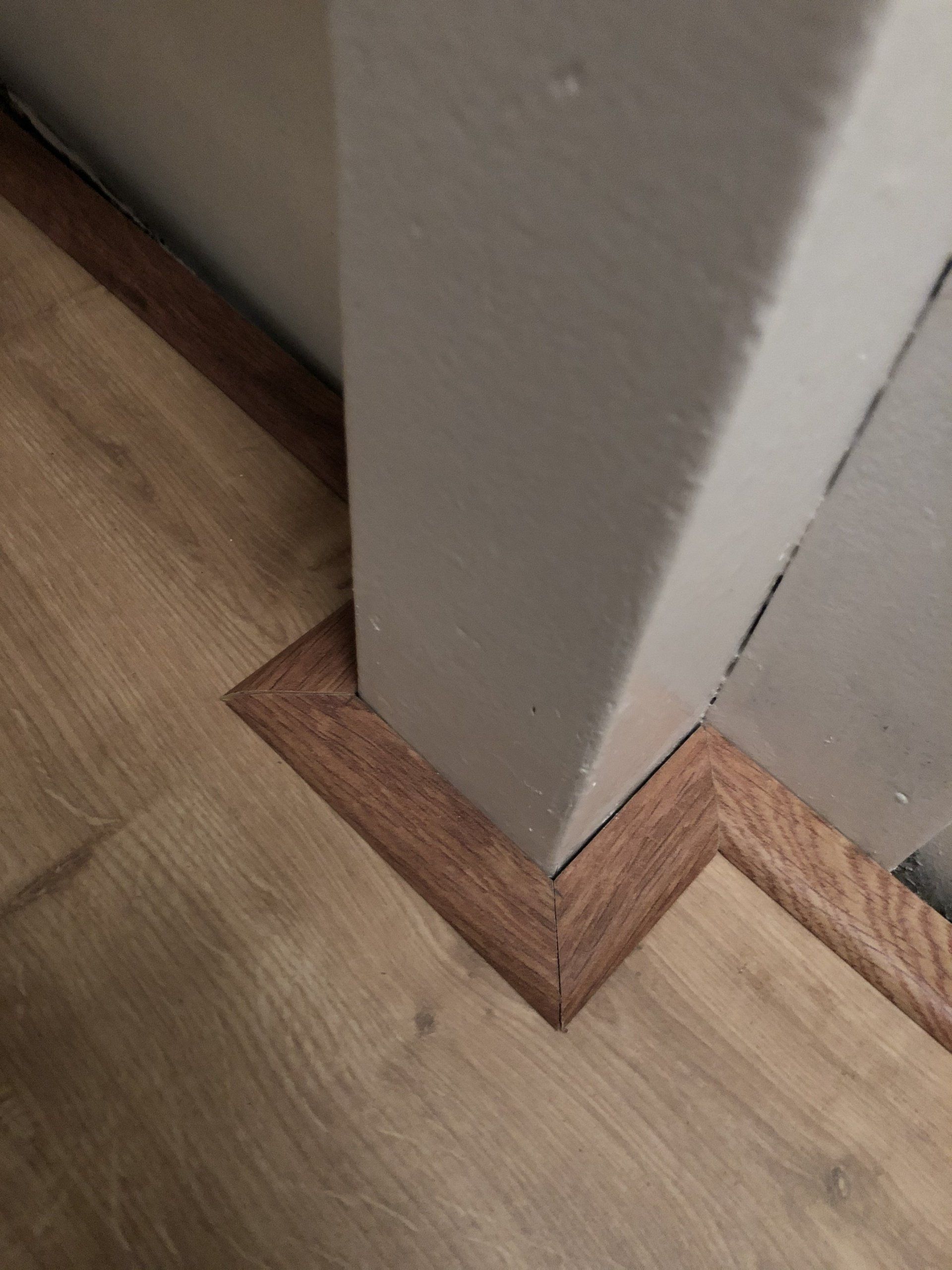 Houten vloer tegen een beige muur, afgewerkt met een bruine plint.
