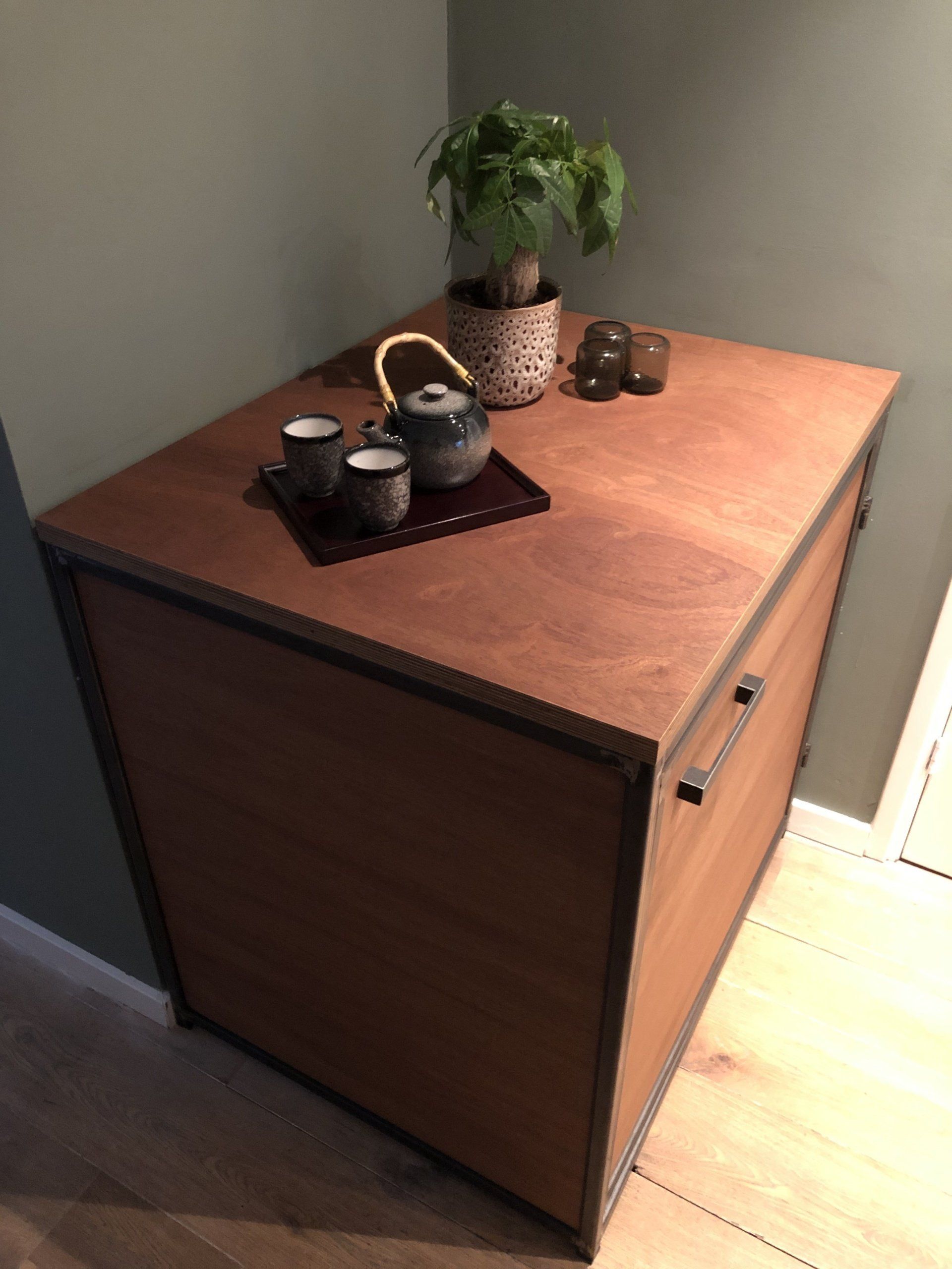 Houten kast met theeservies en een potplant erop.