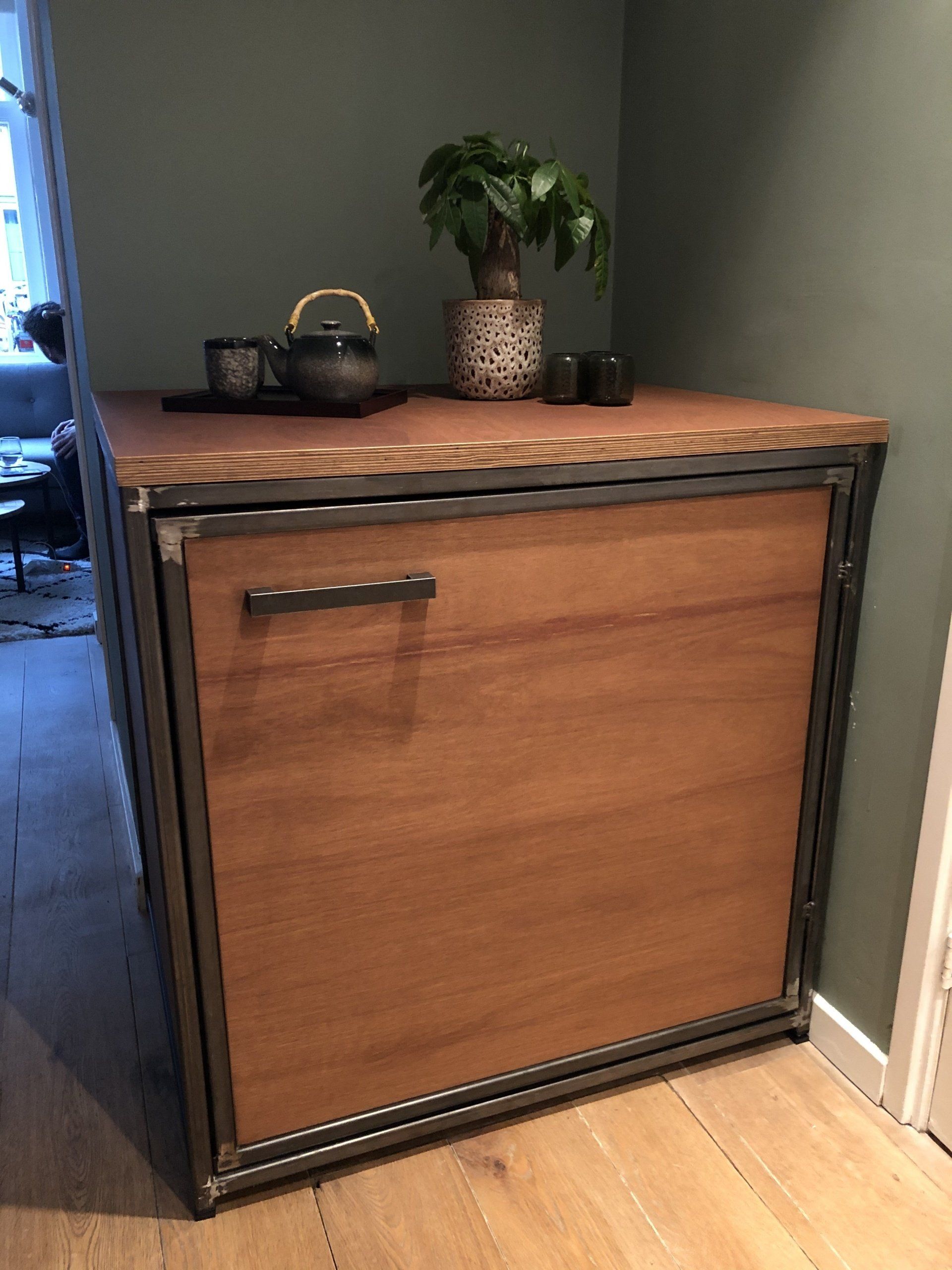 Houten kast met metalen frame; plant, theepot en kopjes erop, binnen.