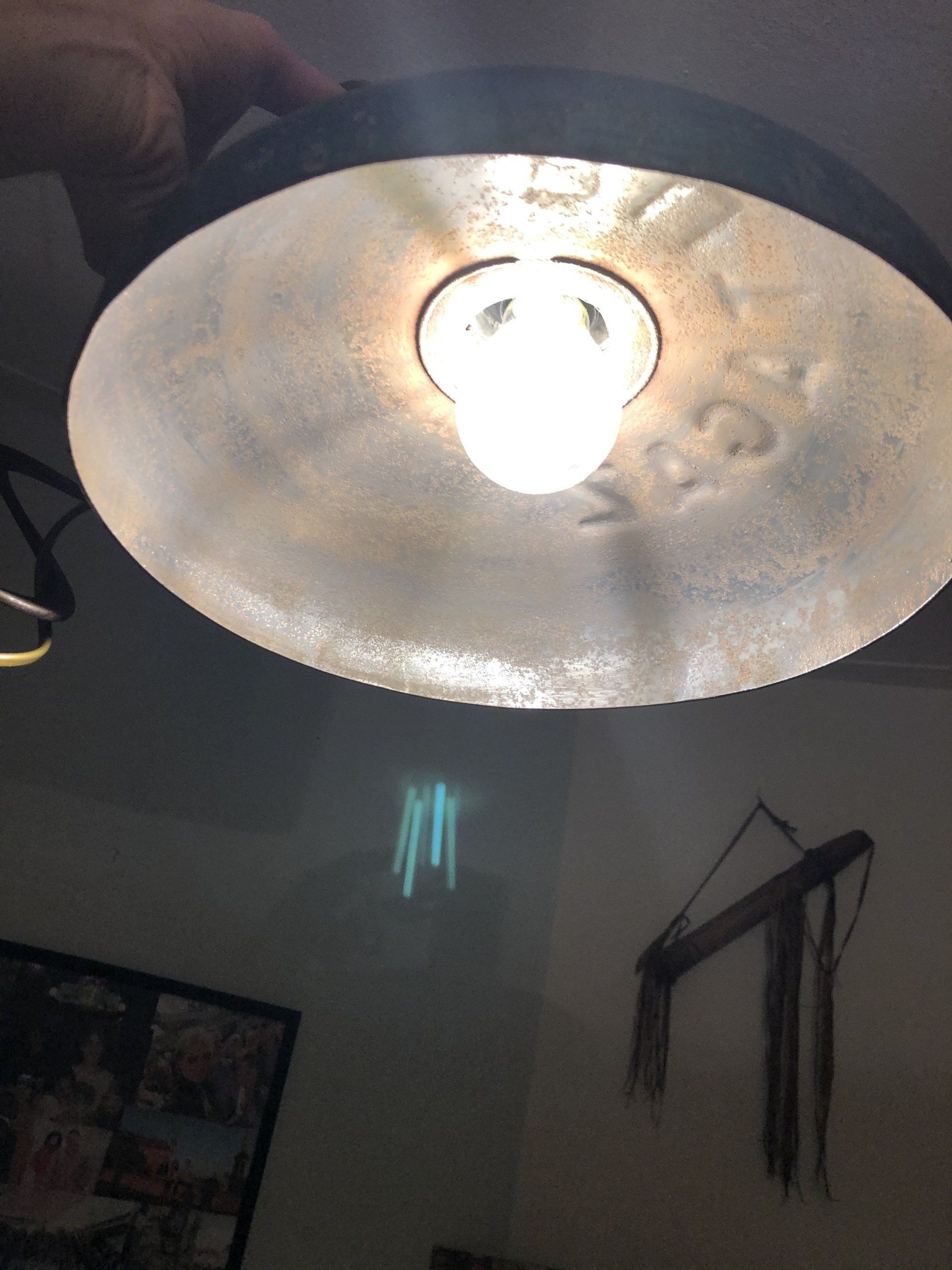 Een felle plafondlamp, in de hand gehouden, werpt licht op een muur met hangende decoraties.