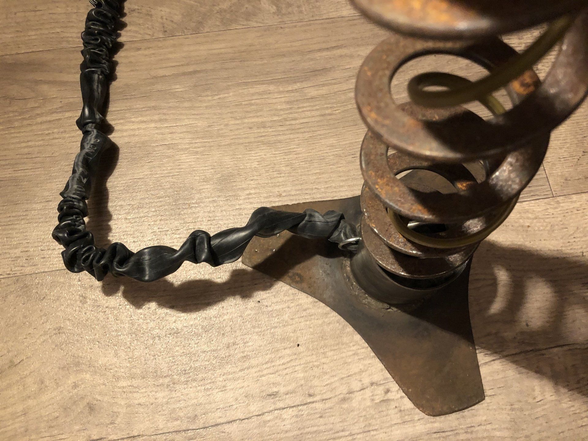 Detailopname van een verroeste metalen veerbasis met een zwart, koordachtig onderdeel eraan bevestigd.