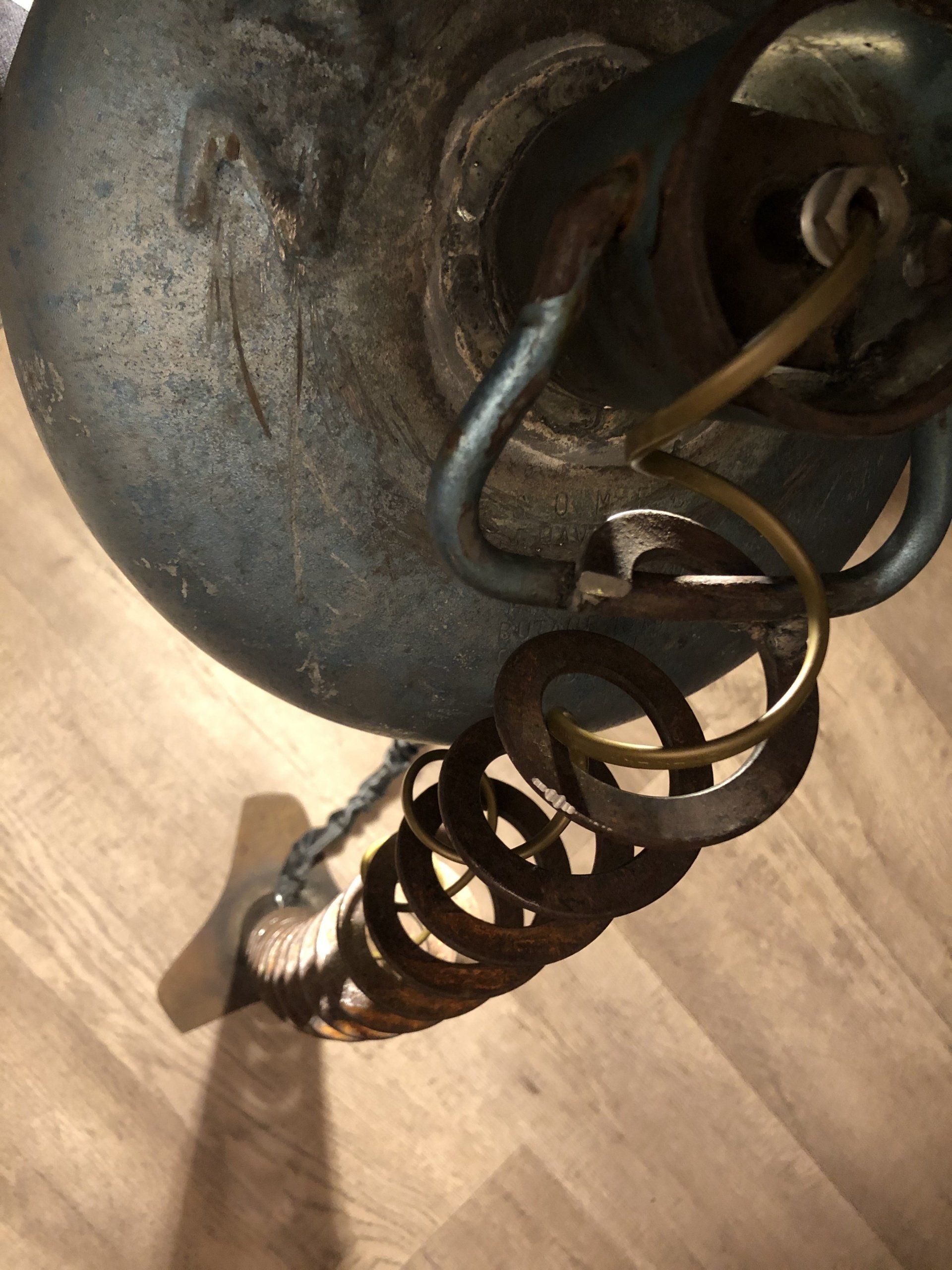 Detailopname van een metalen lamparmatuur, met een ketting, opgerolde draad en een blauwgrijze kap.