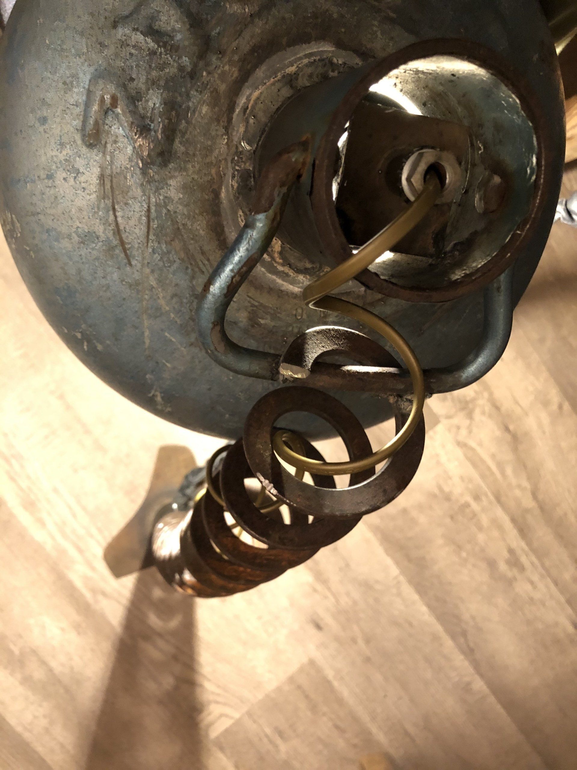 Close-up van een verweerde metalen lampvoet, met een opgerolde goudkleurige kabel die naar beneden loopt.