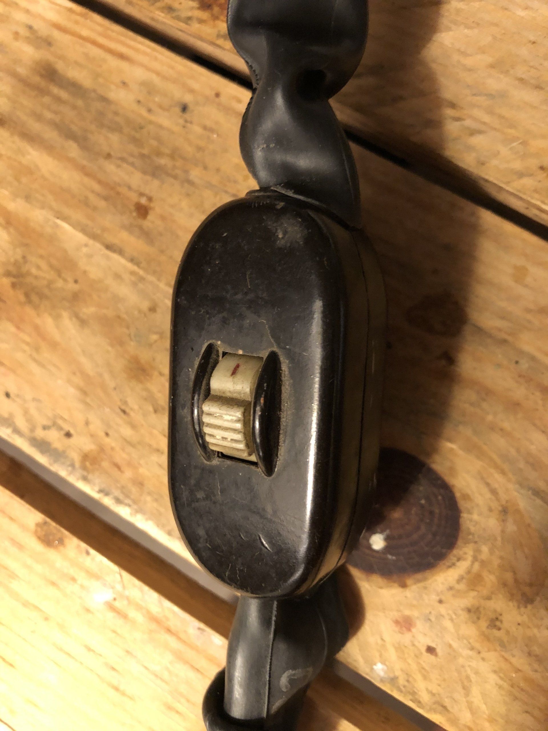 Zwarte inbouwlichtschakelaar met tuimelschakelaar aan een zwart snoer, op een houten ondergrond.