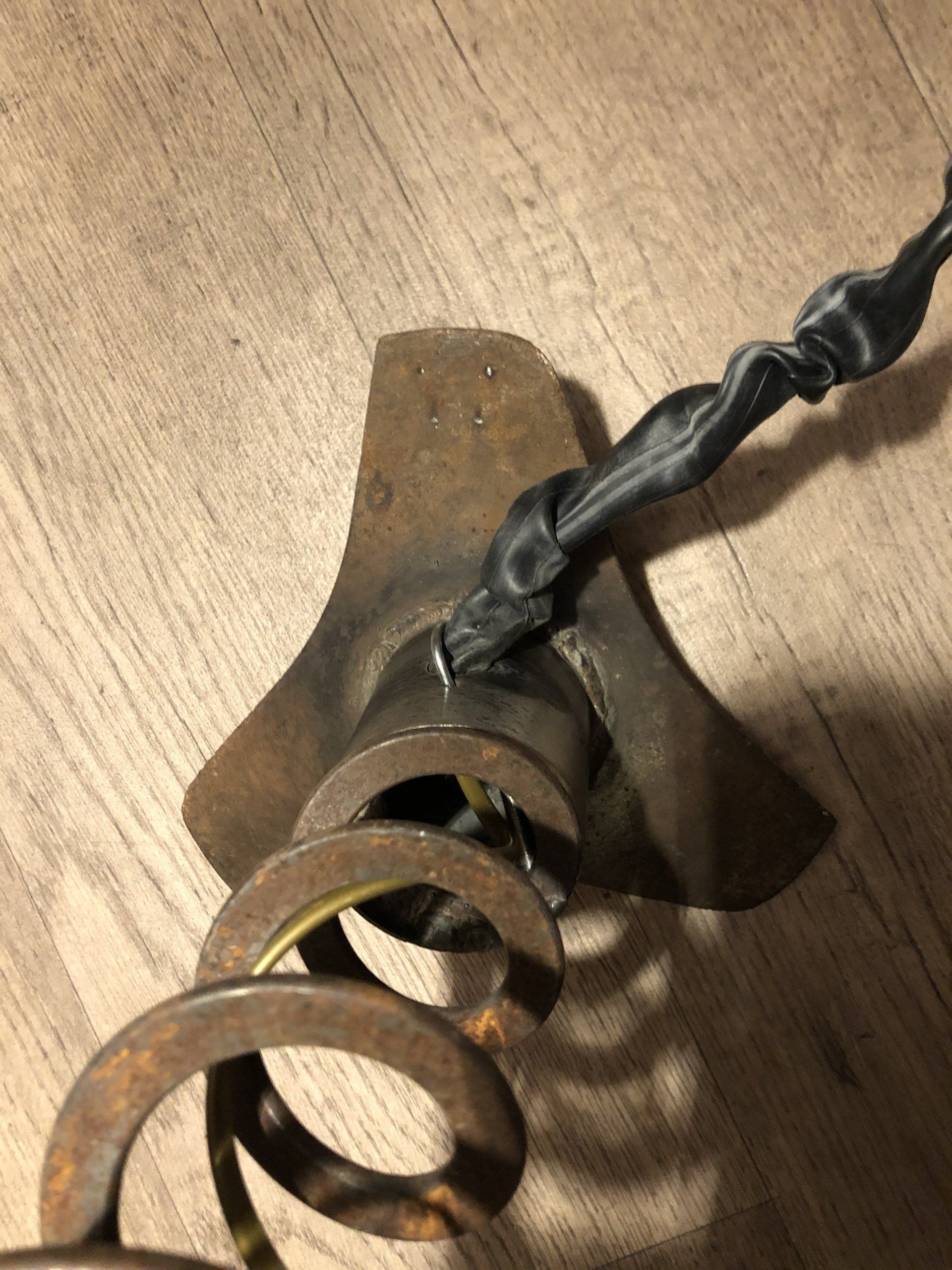 Roestige metalen grondboor met een spiraalveer en een aangesloten elektriciteitssnoer.