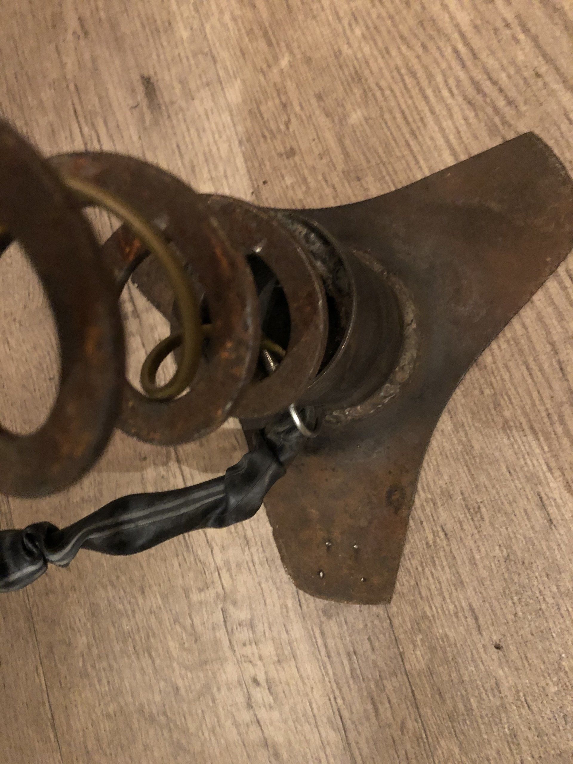 Een roestige metalen veer en plaat, met een zwarte draad eromheen gewikkeld.