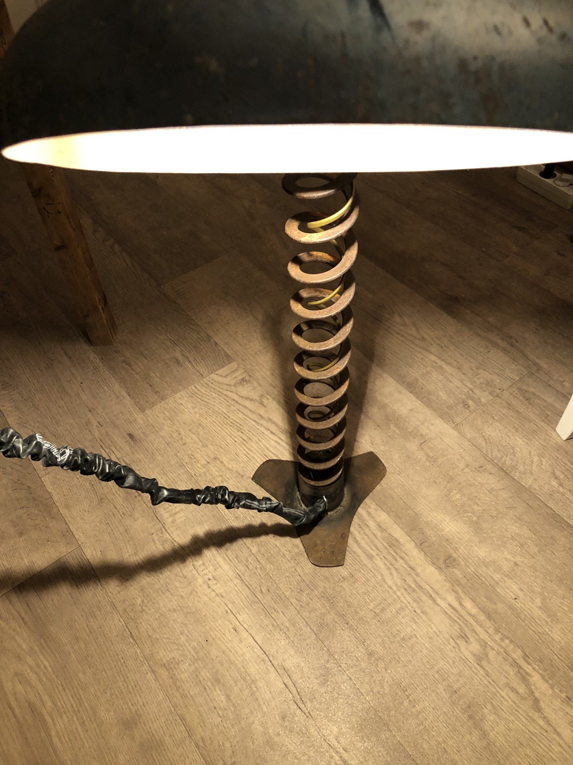 Een decoratieve lamp met een spiraalvormige voet en een donkere kap, die op een houten vloer staat.