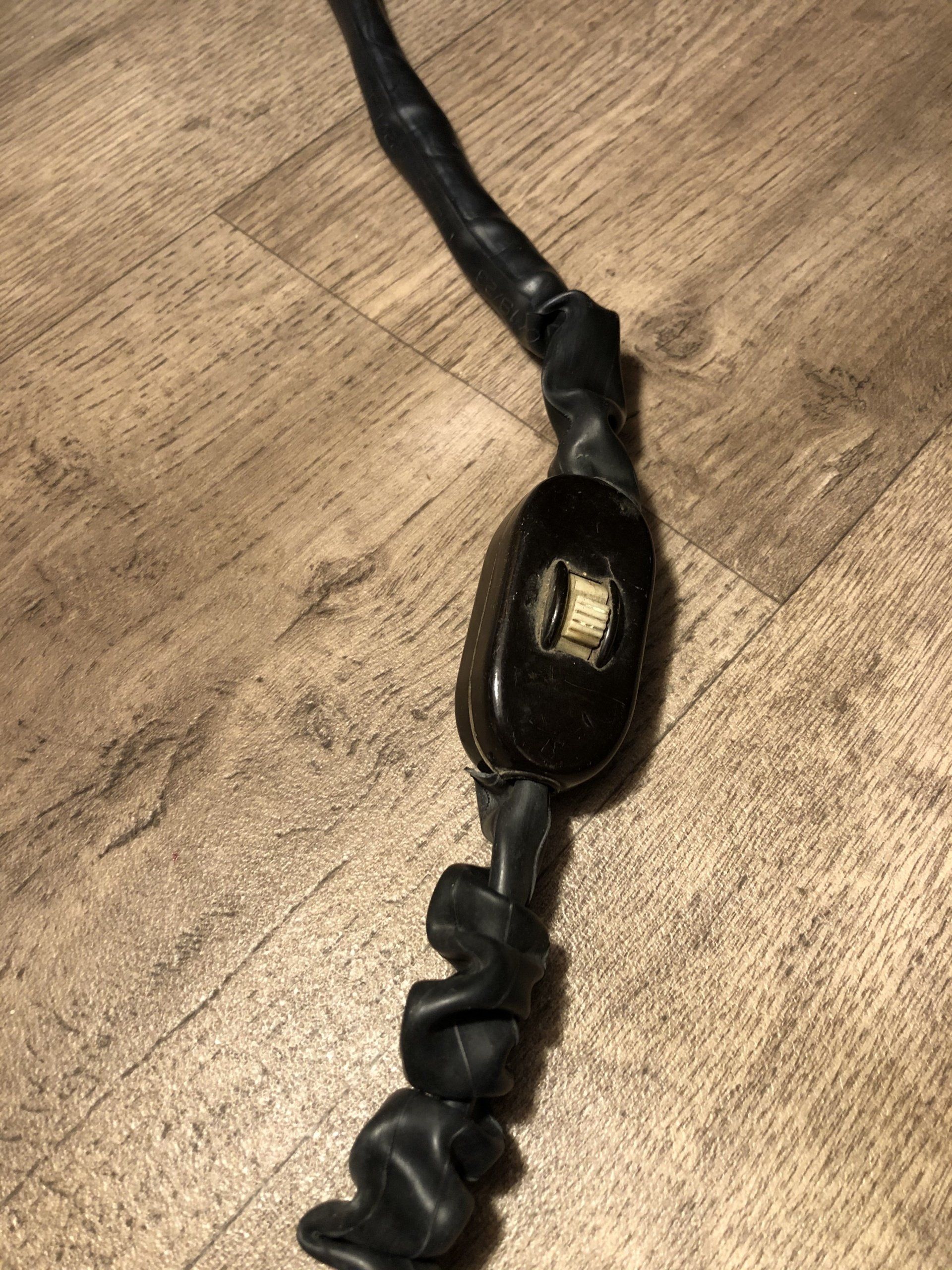 Zwart elektriciteitssnoer met een aan/uit-schakelaar op een houten vloer.