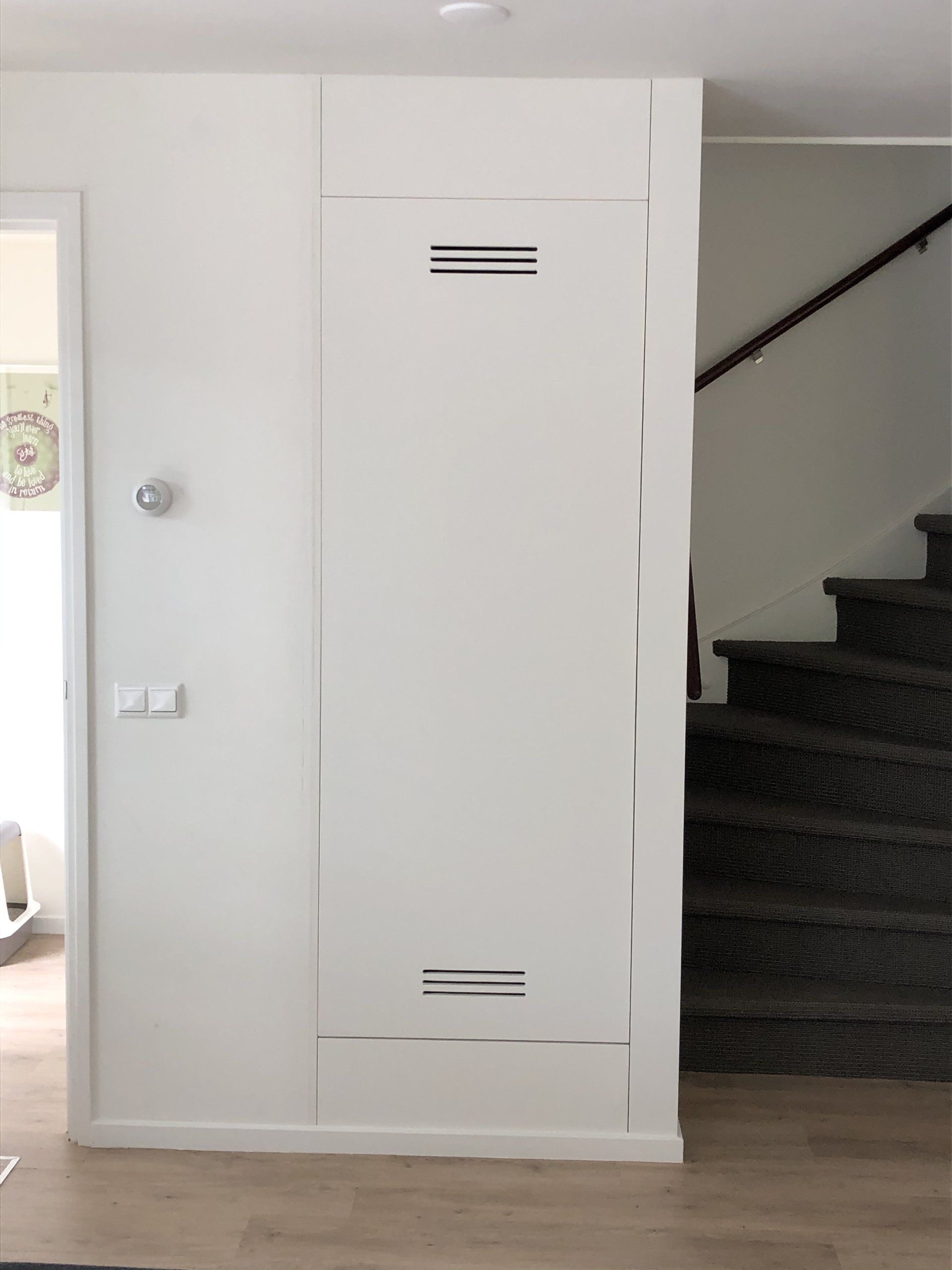 Witte rechthoekige deur met ventilatiesleuven, naast een trappenhuis.