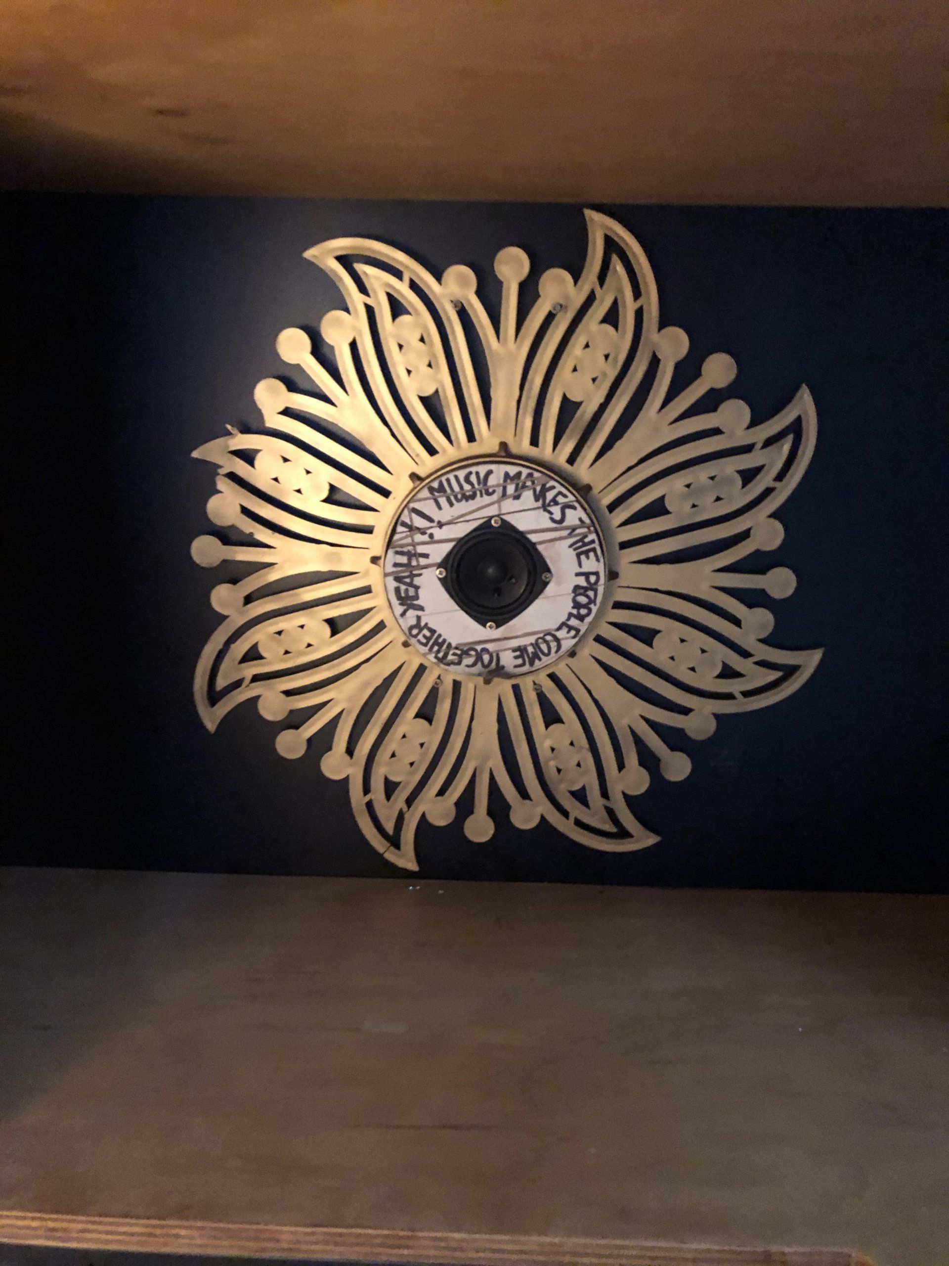 Gouden bloemenwanddecoratie met centrale tekst op een donkerblauwe muur.